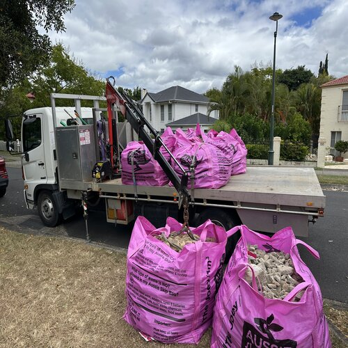 Flatbed truck collecting heavy-duty skip bags filled with landscaping and earthworks waste in a Brisbane suburb.