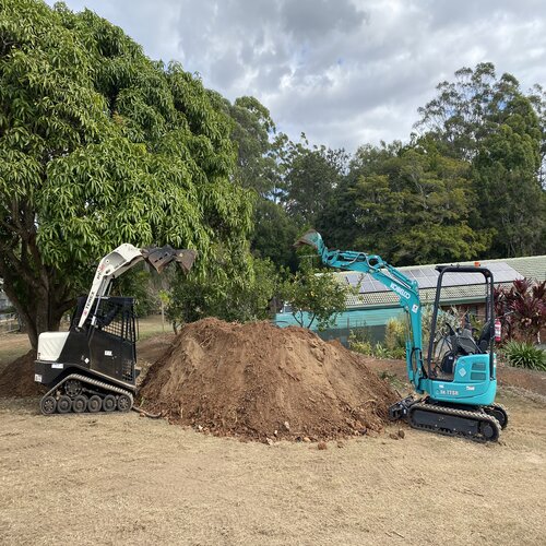 Mini excavator and skid steer loader moving a large soil pile on a landscaping and earthworks site in a residential area.